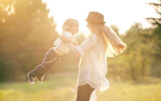 Kobieta bawiąca się z dzieckiem na słońcu – symbol świadomego planowania płodności i możliwości macierzyństwa dzięki zabezpieczeniu komórek jajowych.