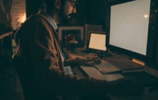 Mężczyzna pracujący nocą przy komputerze w zaciemnionym pomieszczeniu. Praca zmianowa jako czynnik zaburzający sen, rytm dobowy i męską płodność.